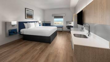 Ein modernes Hotelzimmer mit einem großen Bett, einem kleinen Schreibtisch, einer integrierten Spüle und einem Fenster mit Blick auf die Stadt.
