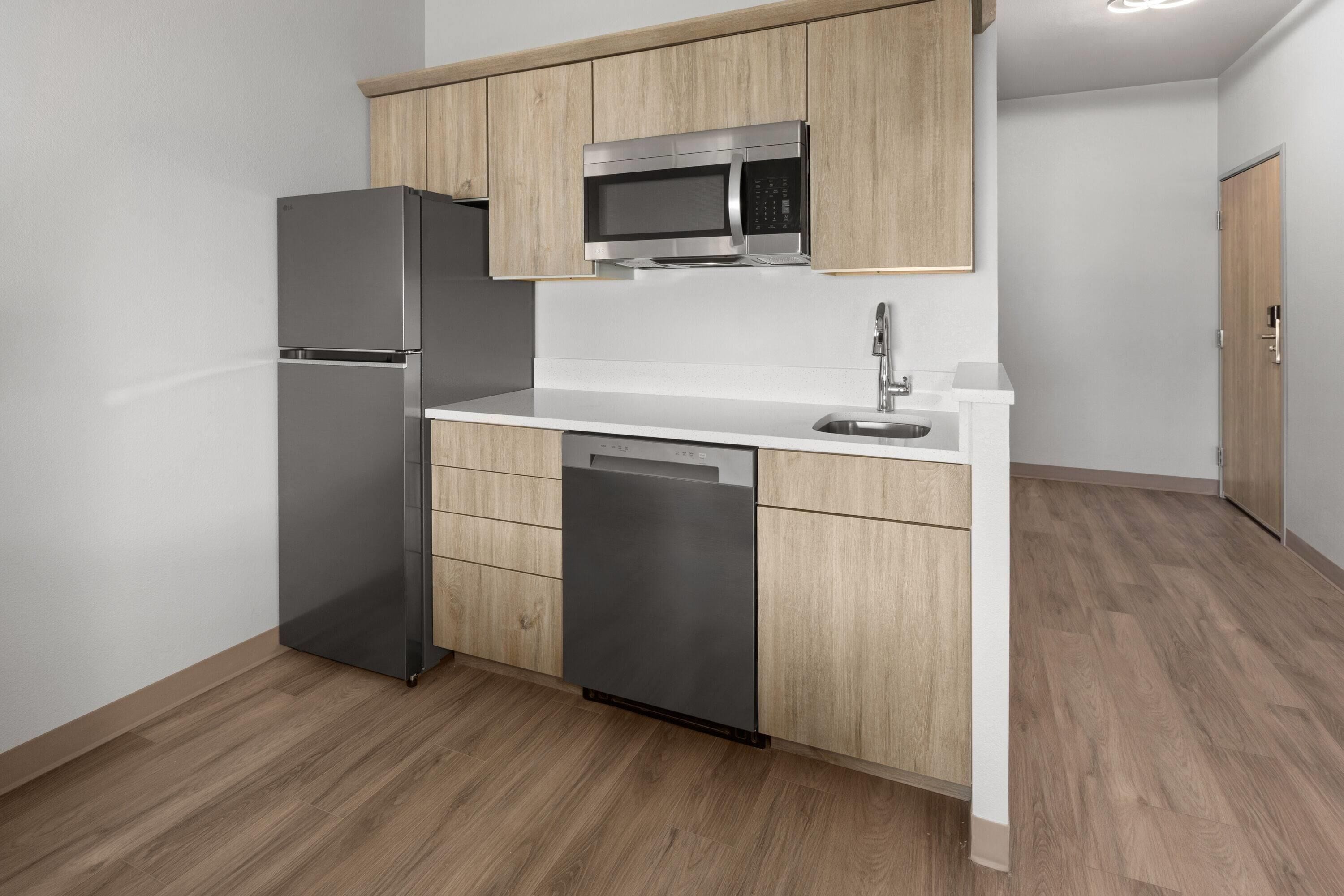 A modern kitchen with stainless steel appliances, wooden cabinets, and a white countertop.