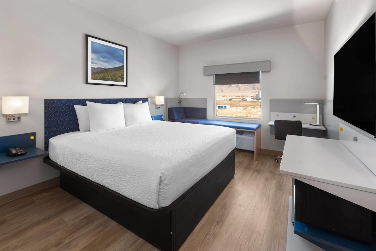 A modern hotel room with a large bed, a desk, a chair, and a TV.