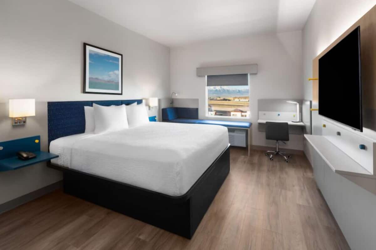 A modern hotel room with a large bed, a desk, a flat-screen TV, and a window with a mountain view.