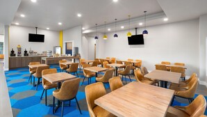 Un comedor moderno con varias mesas y sillas, una barra con estación de bebidas y un televisor de pantalla plana en la pared.