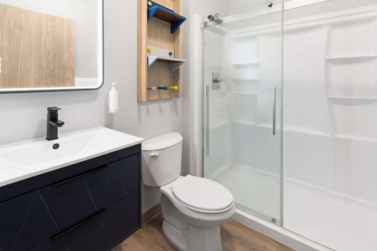 Uma casa de banho moderna com lavatório branco, armários escuros, sanita e cabine de duche com portas de vidro.