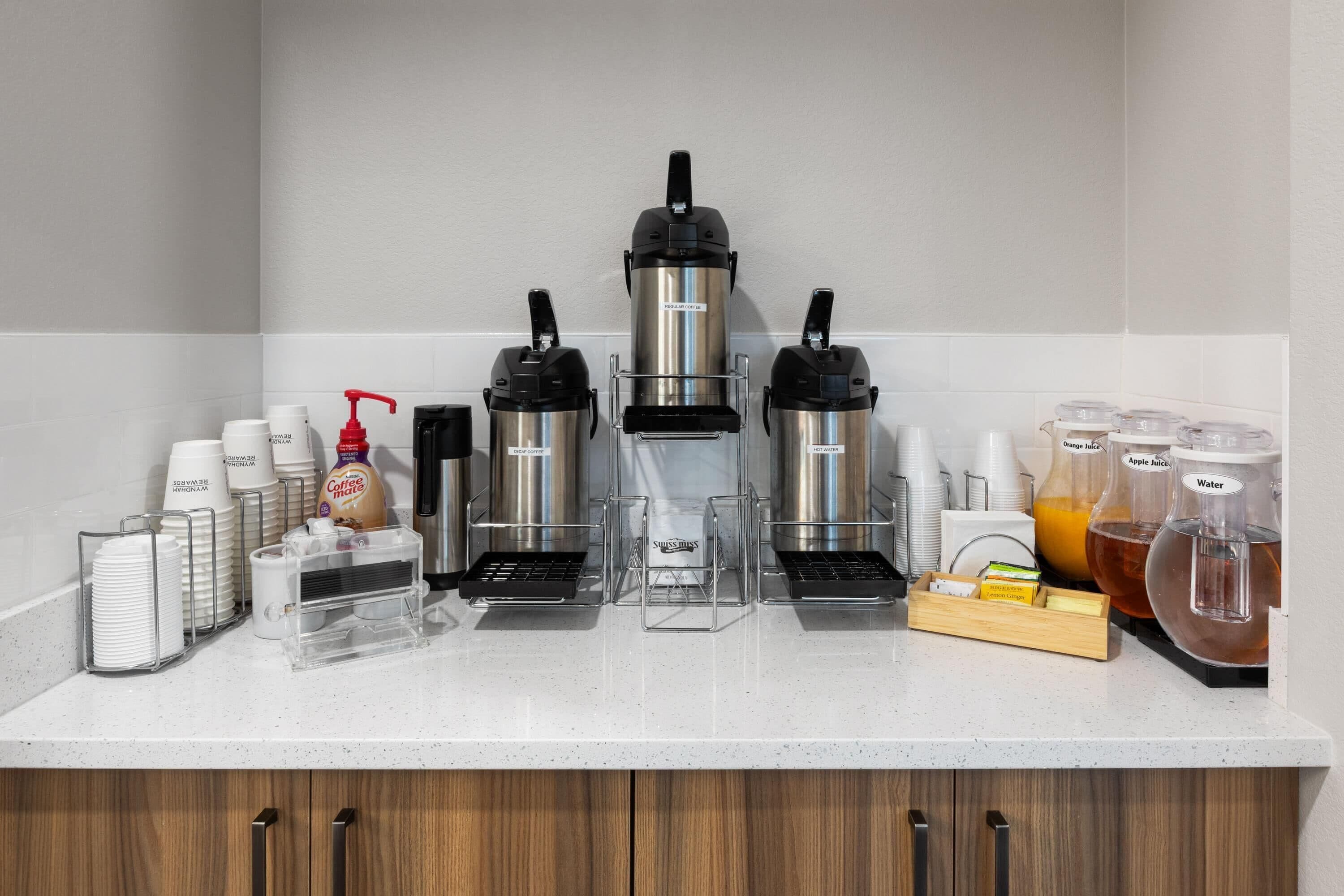 A coffee station with multiple coffee makers, a coffee dispenser, and various coffee cups and containers.