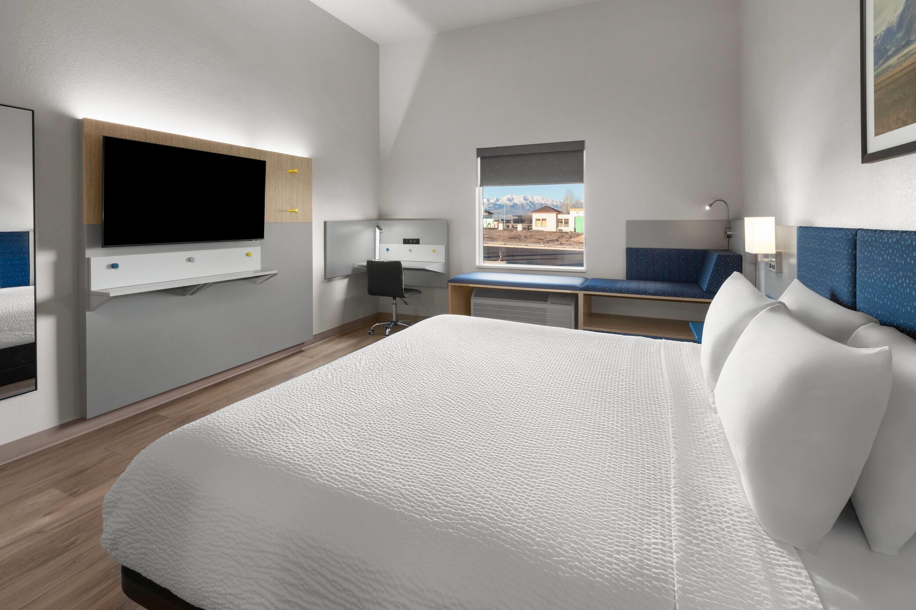 Une chambre d’hôtel avec un grand lit, un bureau, une chaise, un téléviseur fixé au mur, une fenêtre donnant sur les montagnes et une lampe.