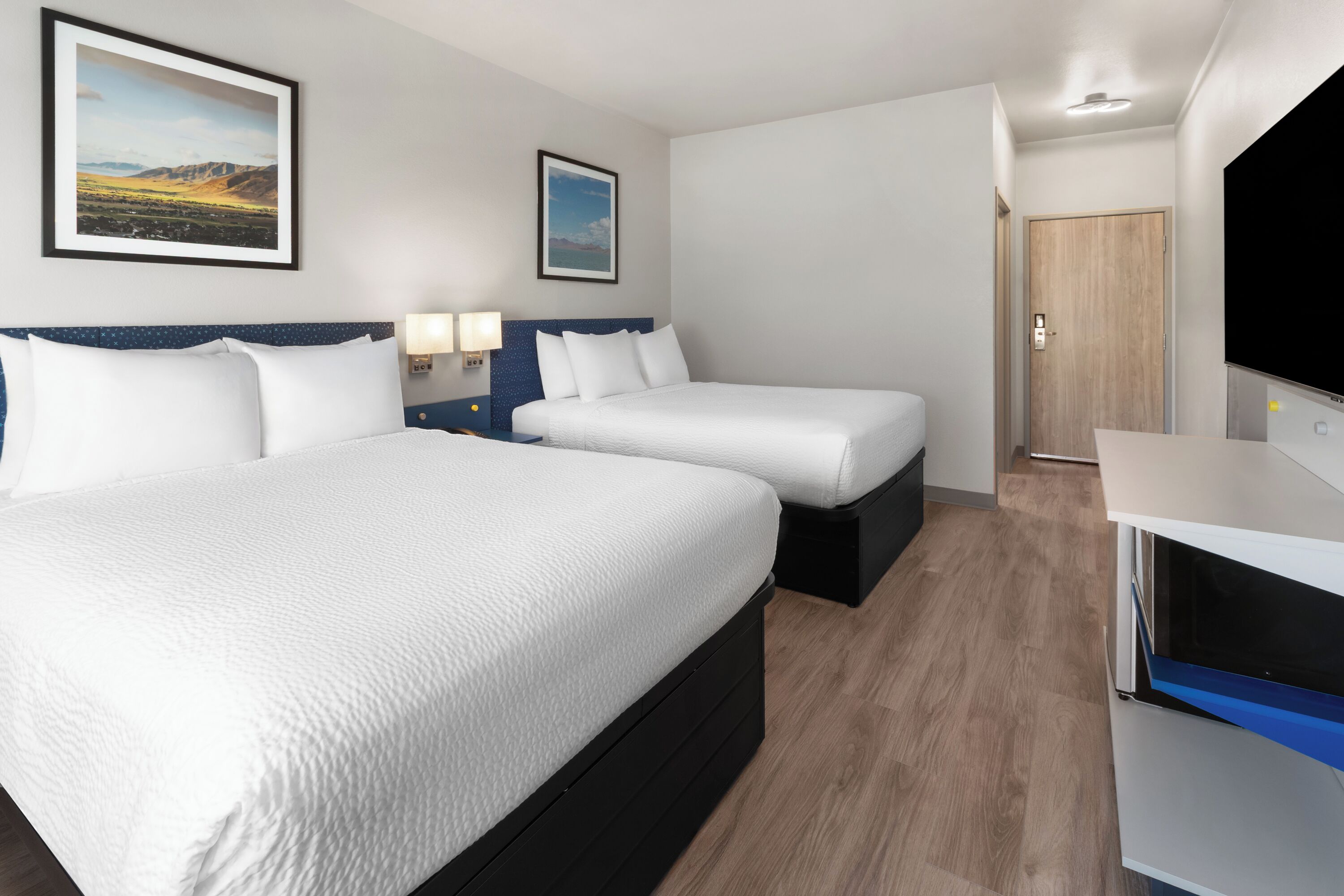 Une chambre d’hôtel avec deux lits, une télévision et une porte donnant sur une autre pièce.