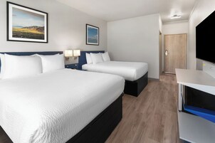 Habitación de hotel con dos camas, una televisión y una puerta que da a otra habitación.