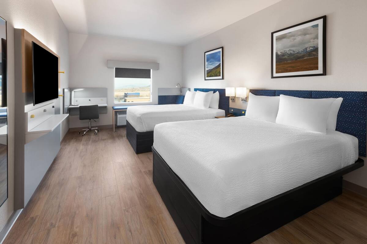 A hotel room with two beds, a desk, a chair, a TV, and a window with a view.