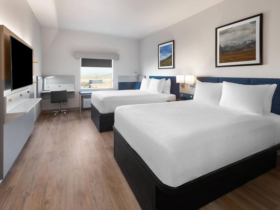 A hotel room with two beds, a desk, a chair, a TV, and a window with a view.