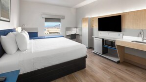 Una habitación de hotel moderna con una cama grande, un escritorio, un televisor de pantalla plana, un microondas y un lavamanos.