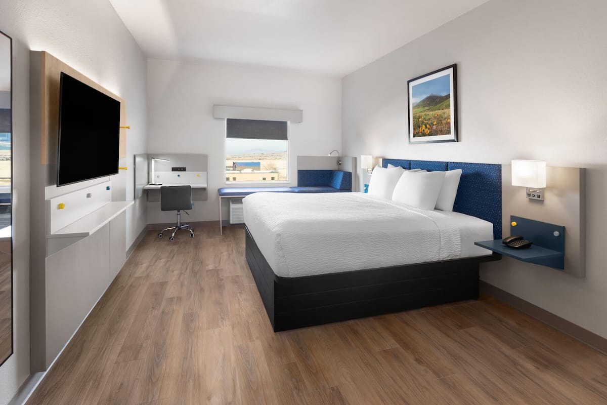 A hotel room with a large bed, a desk with a computer, a TV, and a window with a view of the outdoors.