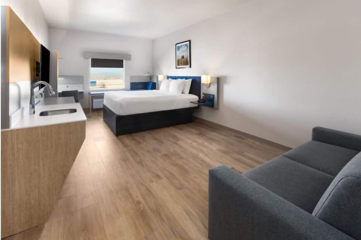 A modern hotel room with a bed, bedside table, lamp, and a view of the outdoors.