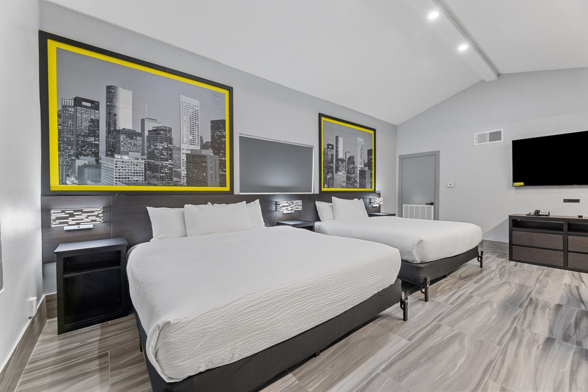Une chambre d’hôtel moderne avec deux lits, une grande télévision et des photos encadrées représentant des vues de la ville, accrochées au mur.