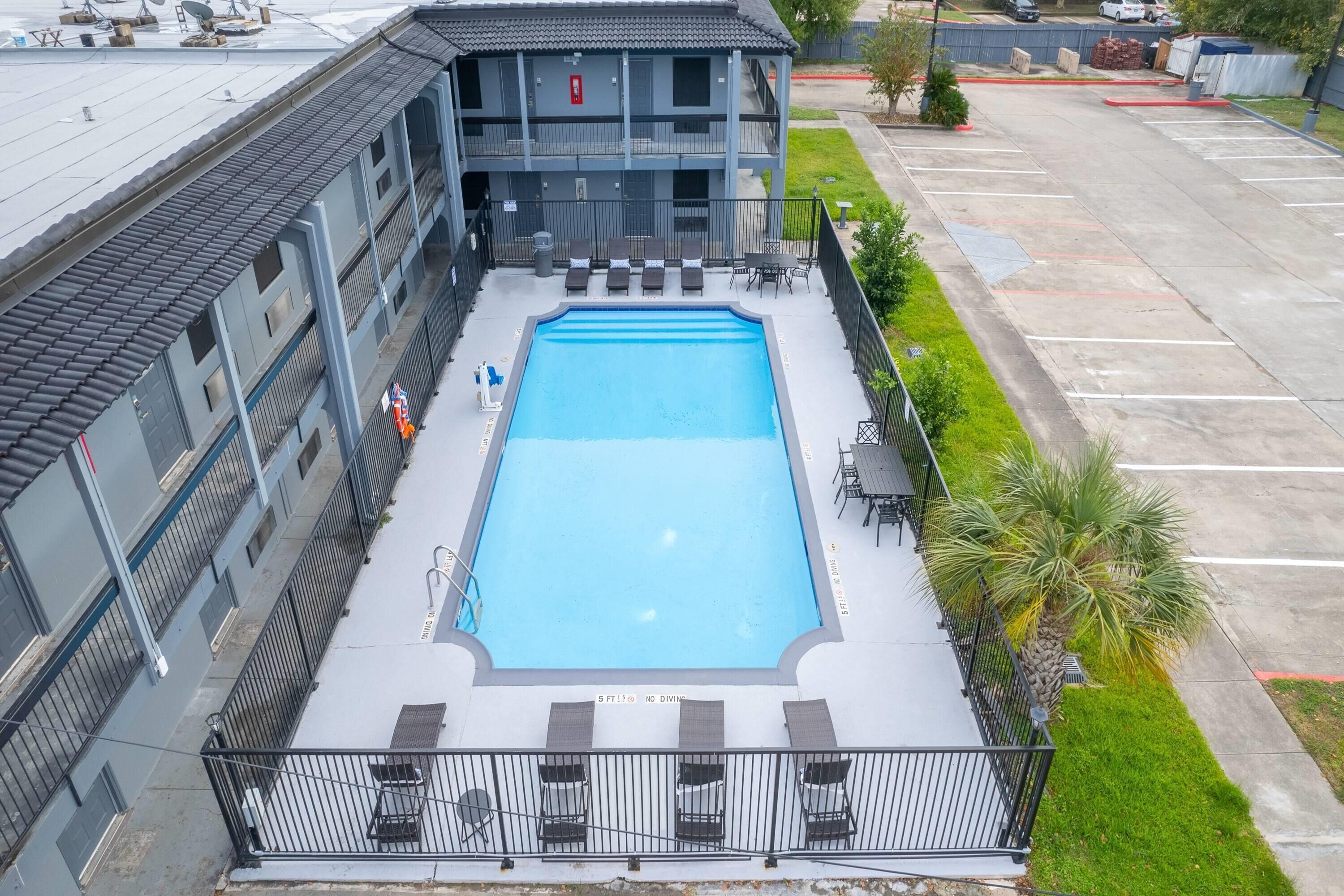 Une piscine sur le toit offrant une vue sur un immeuble à plusieurs étages, une zone délimitée par une clôture et un parking.