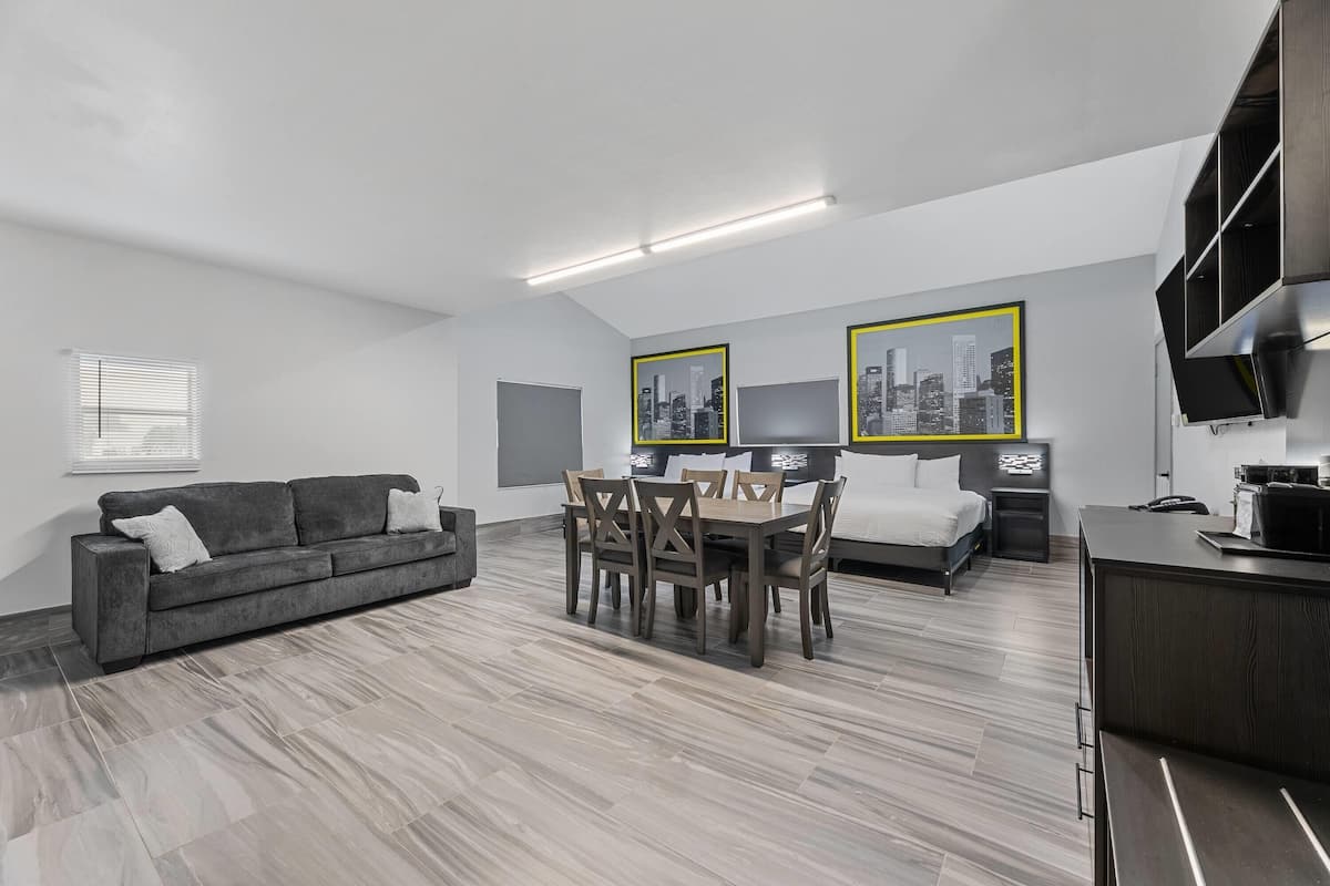 A modern apartment with a living room, dining area, and bedroom. It features a gray sofa, a dining table with chairs, a bed, and a kitchenette.