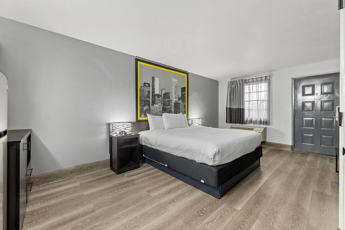 A modern bedroom with a bed, a nightstand, a wall-mounted picture, and a door.