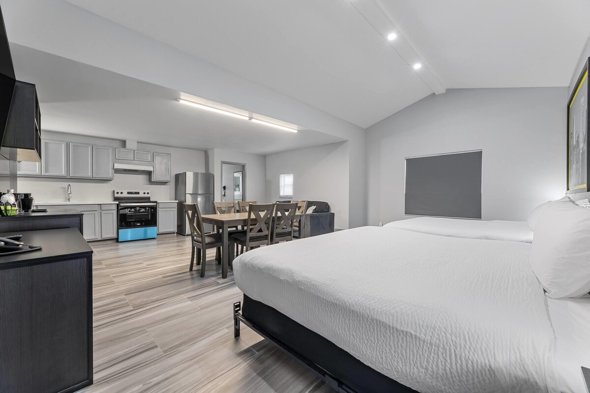 A modern hotel room with a large bed, a desk, and a kitchenette.