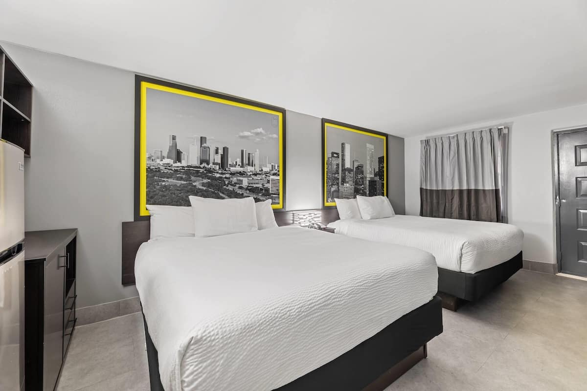 A hotel room with two beds, a television, and two framed cityscape pictures on the wall.