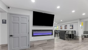 A modern hotel lobby with a flat-screen TV mounted above a fireplace, a reception desk, and a seating area with chairs and tables. - Super 8 by Wyndham Texas City/Galveston Area (Texas City)