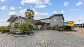 A Super 8 Days Inn with a modern design, featuring a curved driveway and landscaped areas with palm trees and shrubs.