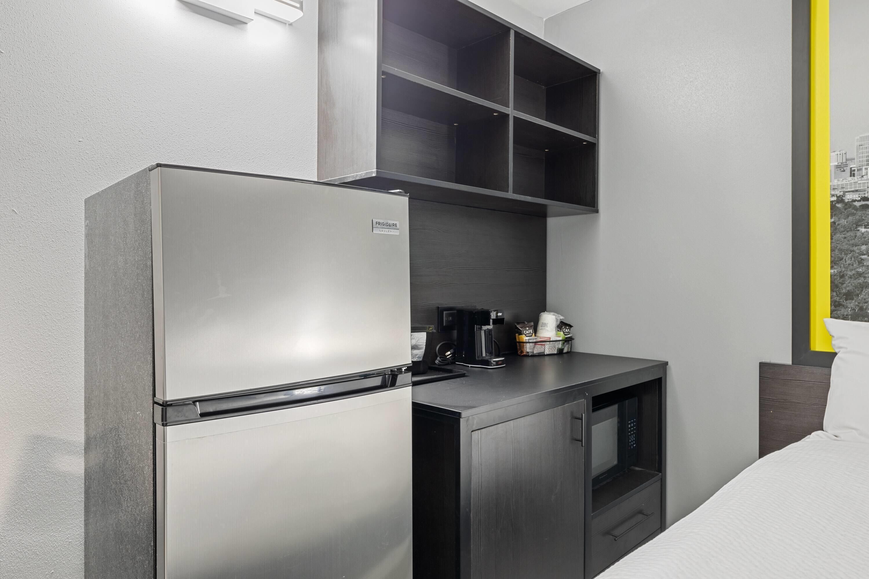 A compact kitchenette with a stainless steel refrigerator, a microwave, and a coffee maker.