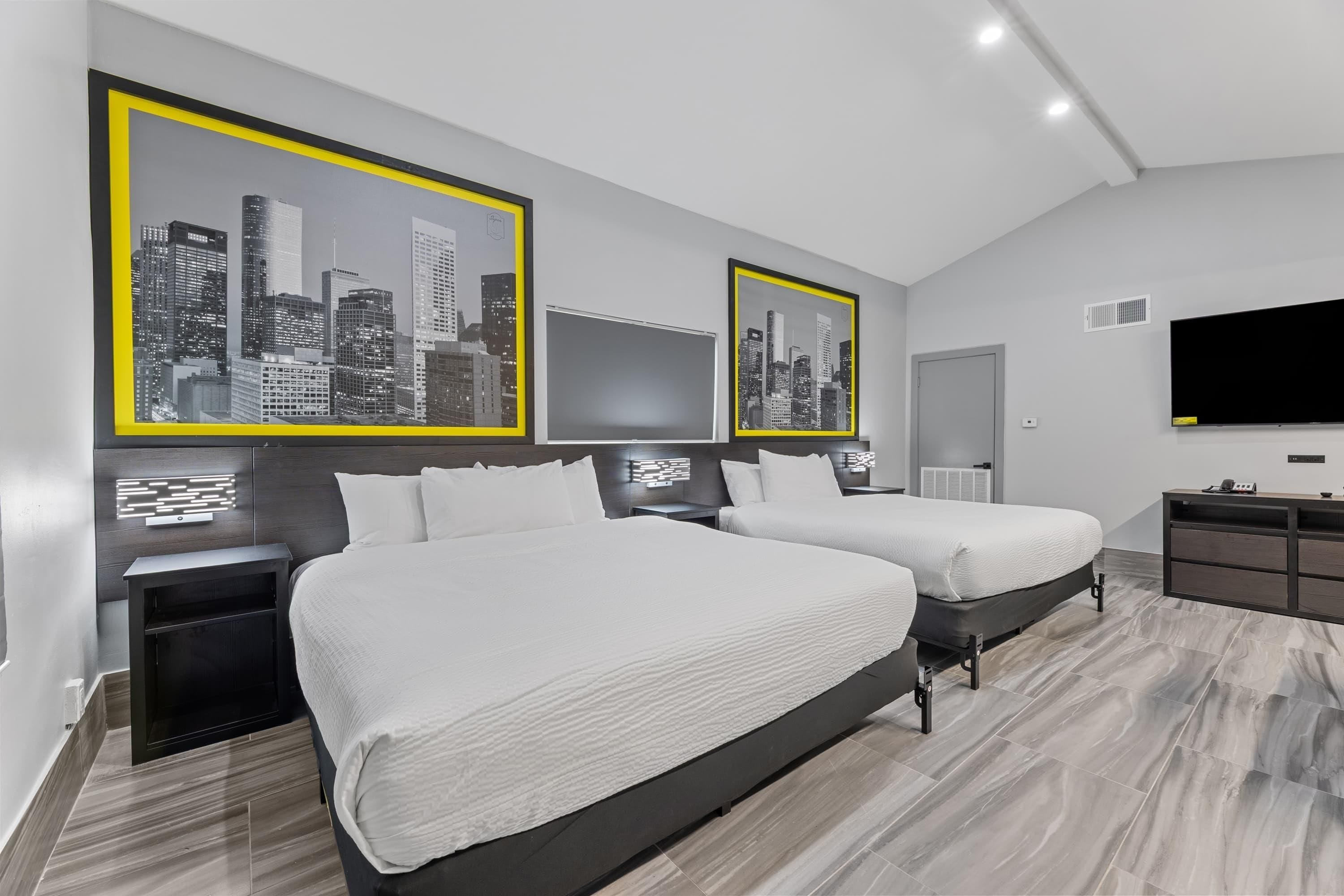 Een moderne hotelkamer met twee bedden, een flatscreen televisie en stadsgezicht kunstwerken aan de wanden.