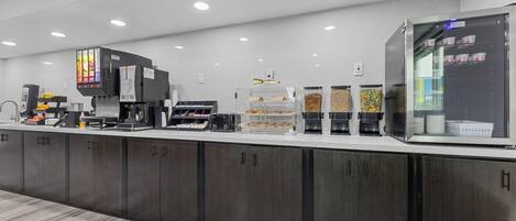 A modern coffee station with multiple coffee machines, a refrigerated display case, and various coffee pods.