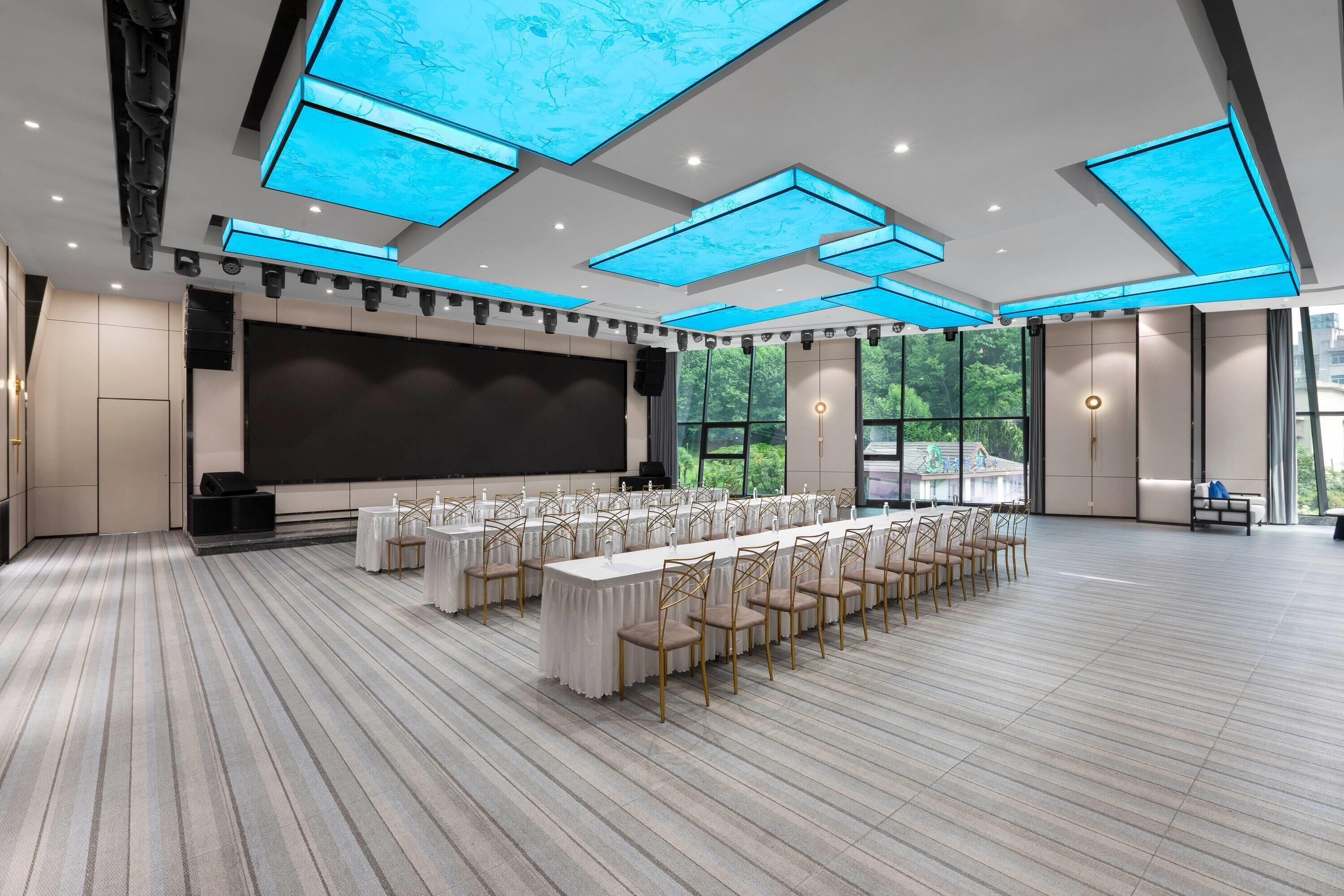 Un salón de conferencias con una mesa larga, sillas, una pantalla grande y tragaluces.