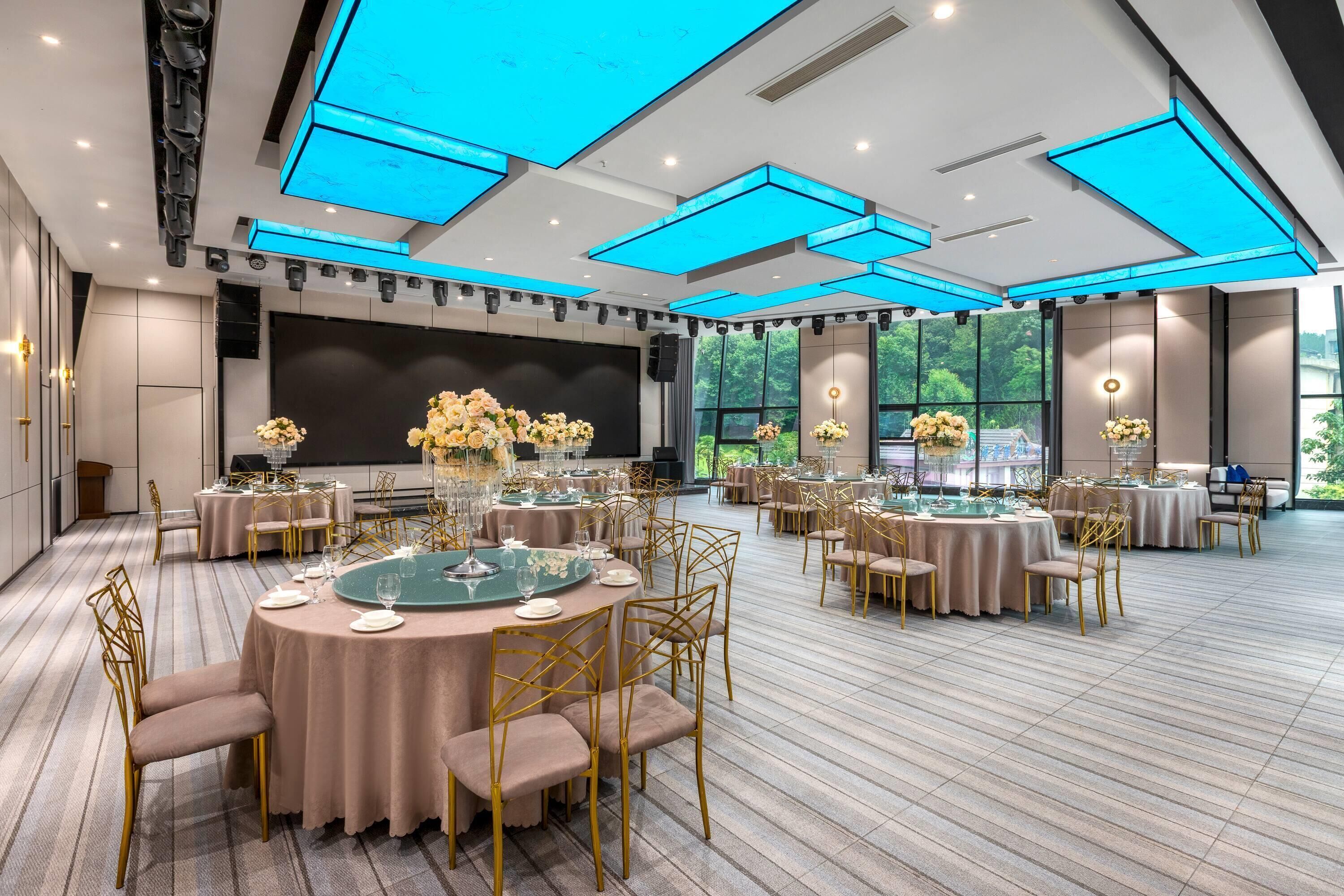 A spacious banquet hall with round tables, gold chairs, and floral centerpieces.