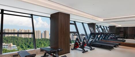 A modern gym with exercise equipment, large windows, and a view of a cityscape.