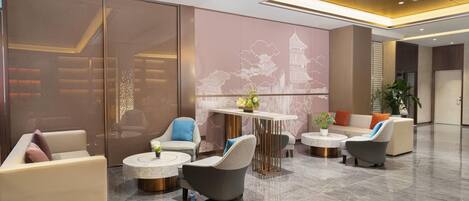 A modern lobby with seating areas, a central table, and a decorative wall with a building outline.