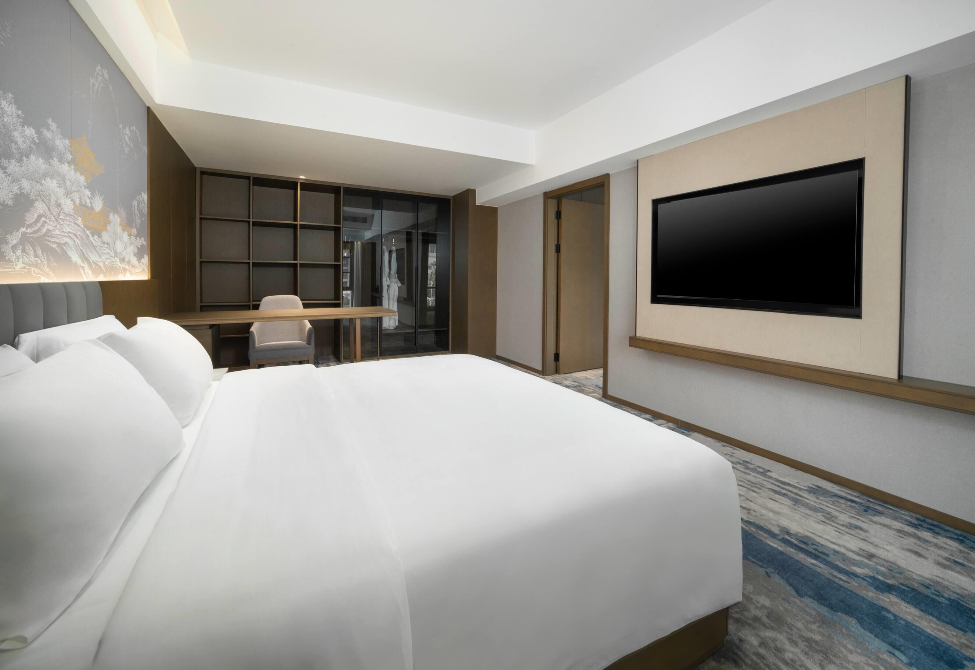 Una habitación de hotel moderna con una cama grande, un escritorio, un televisor y una estantería.