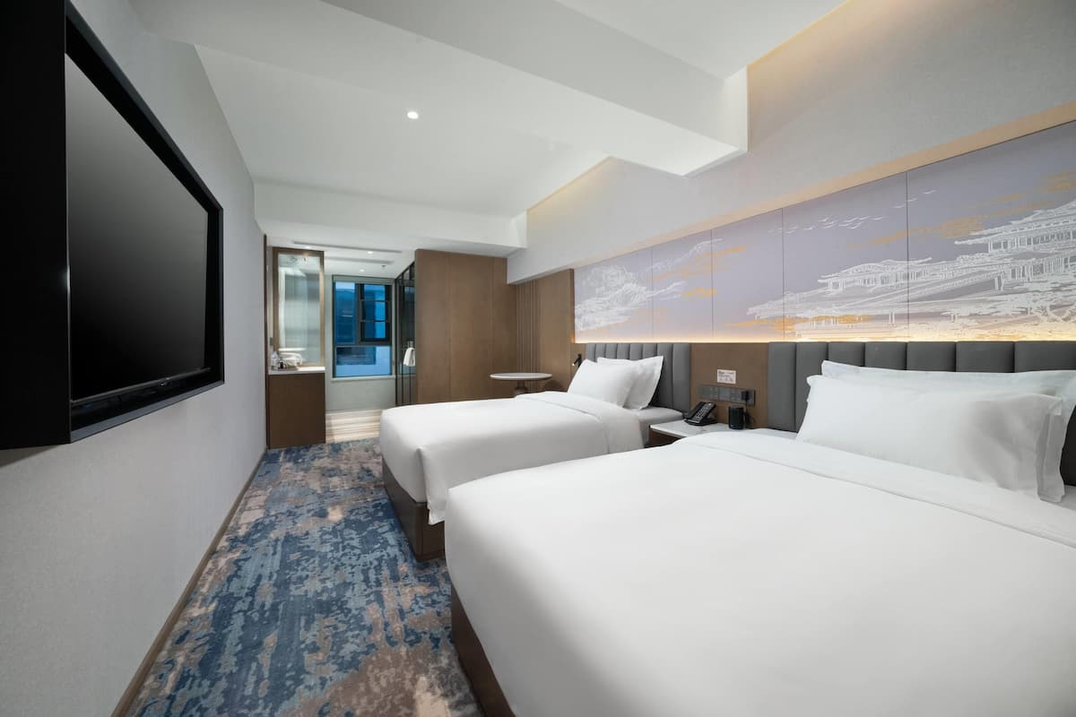 Ein Hotelzimmer mit zwei Betten, einem großen Flachbildfernseher, einem Wandbild und einem blau gemusterten Teppich.