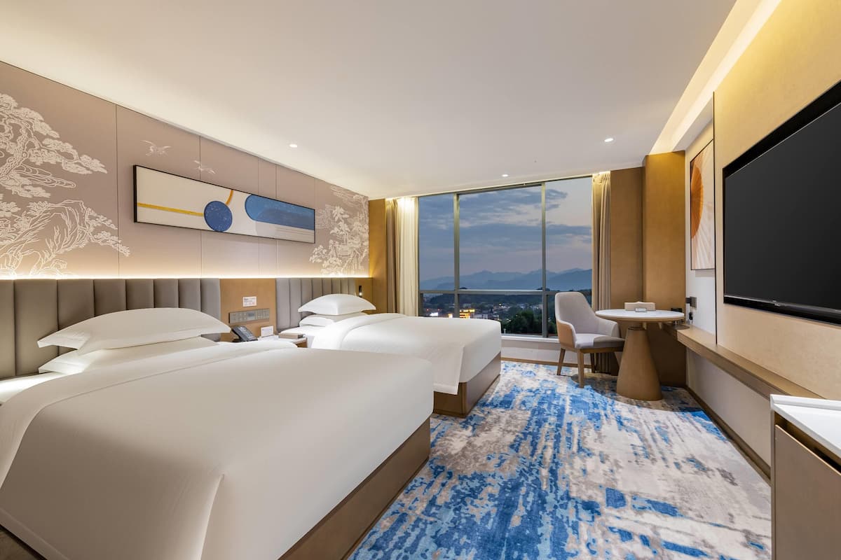 Ein modernes Hotelzimmer mit einem großen Bett, einem Schreibtisch, einem Stuhl, einem Fernseher und Blick auf die Stadt.