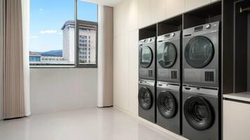 Un moderno lavadero con cuatro lavadoras de carga frontal, amplias ventanas con vista a un paisaje urbano y un diseño limpio y minimalista.