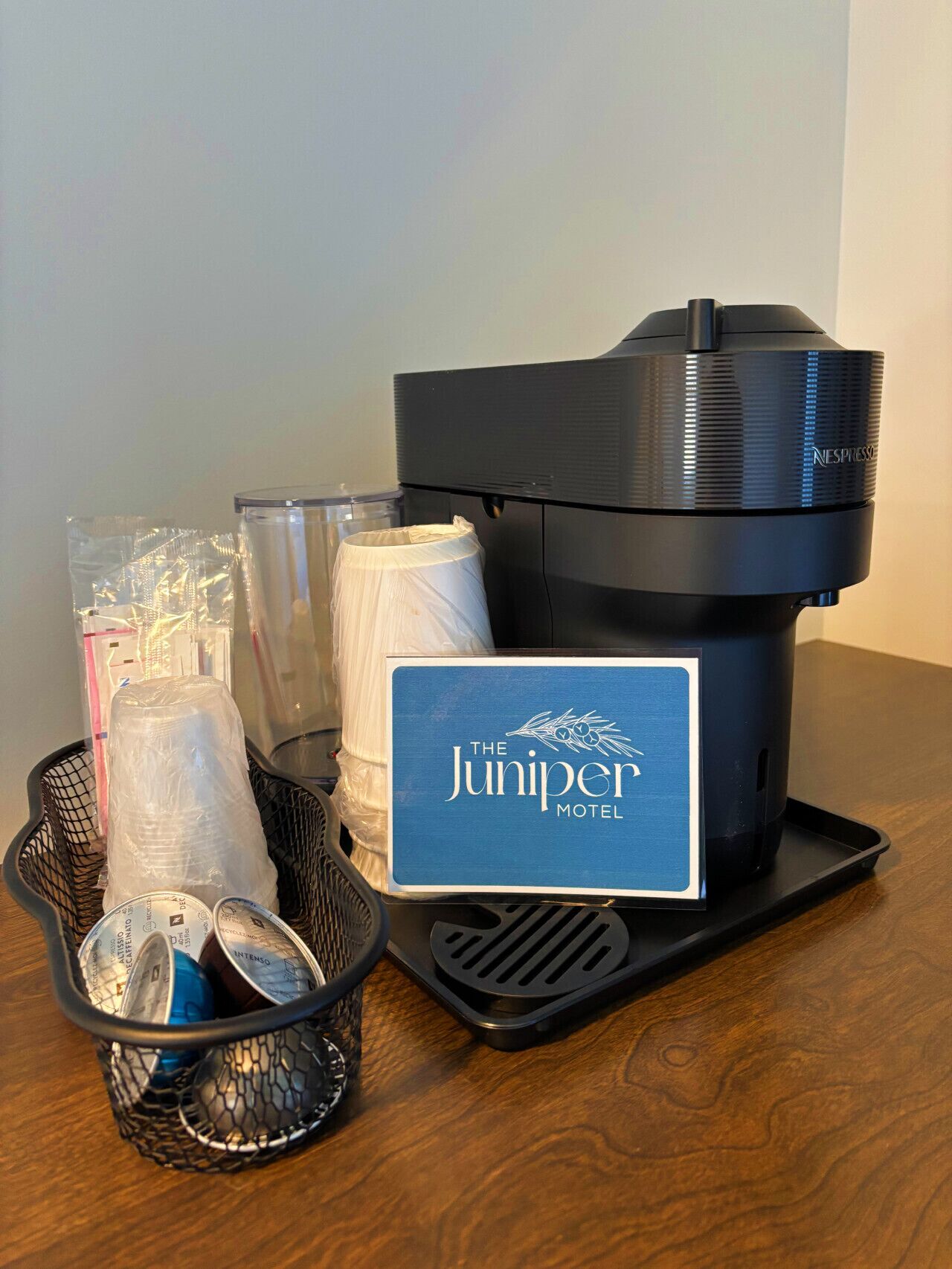 Una máquina de café Nespresso, una cesta con vasos desechables y un cartel que indica The Juniper Motel.