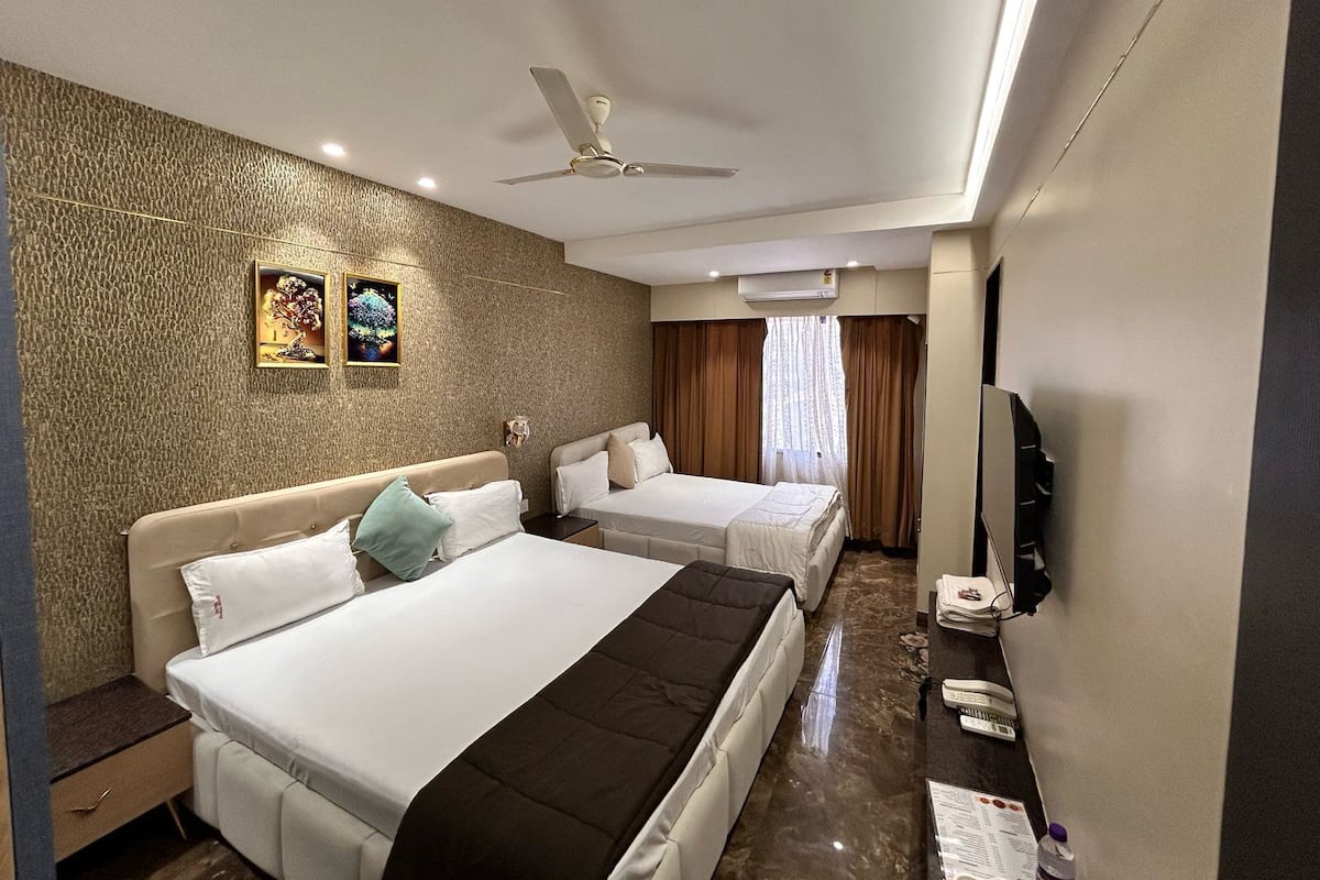 Ein Hotelzimmer mit zwei Betten, einem Deckenventilator, einer Klimaanlage und einem an der Wand befestigten Fernseher.