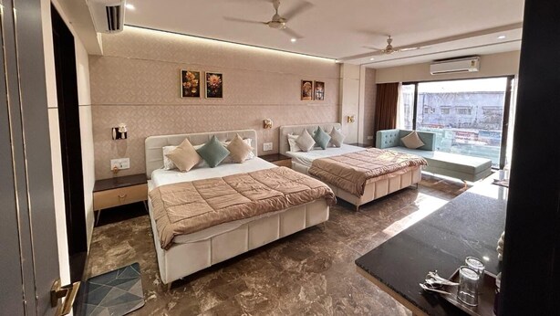 A modern hotel room with two beds, a dining table, and a large window offering a city view.
