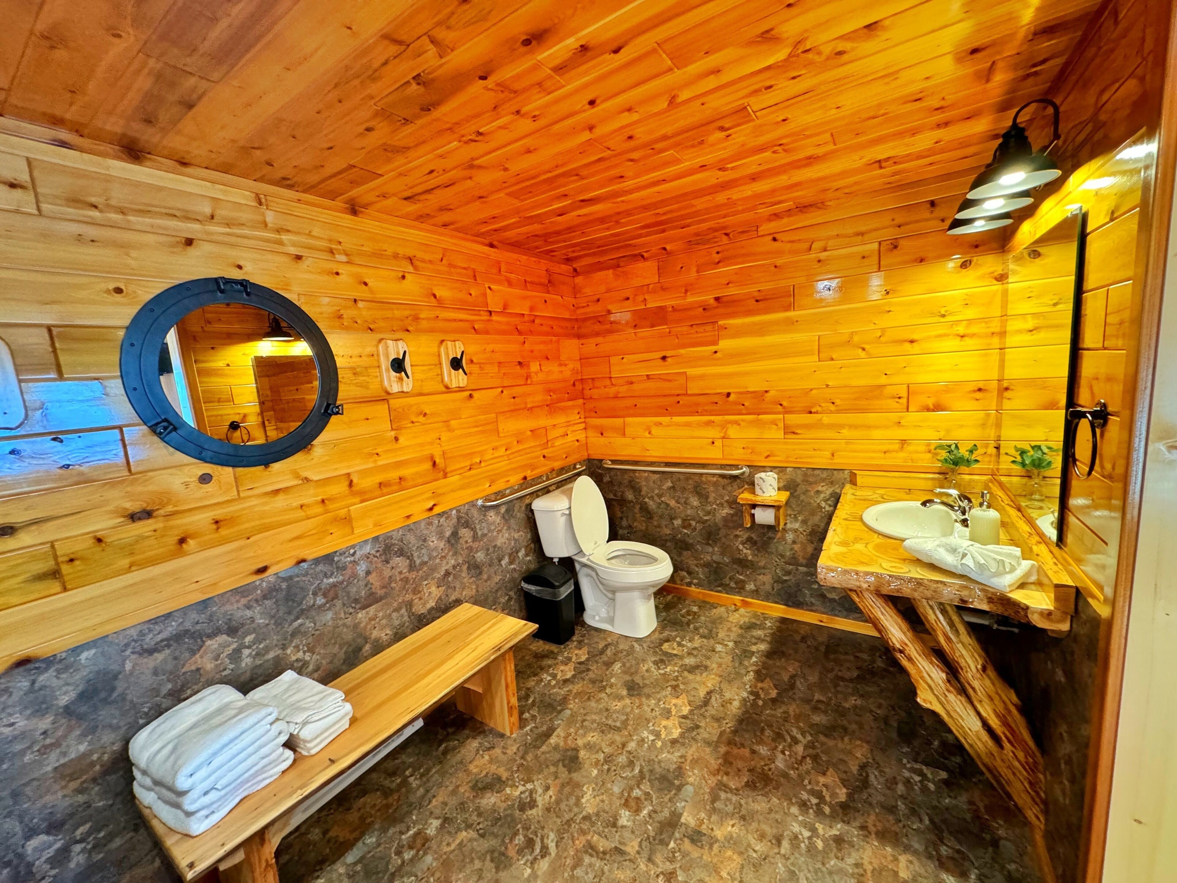 A wooden cabin bathroom with a toilet, sink, bench, and towels.