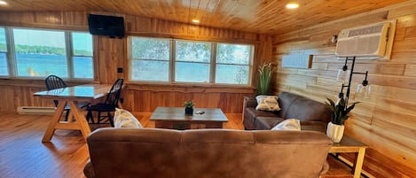 A cozy cabin interior with a wooden ceiling, a sofa, a dining table, and a TV mounted on the wall.
