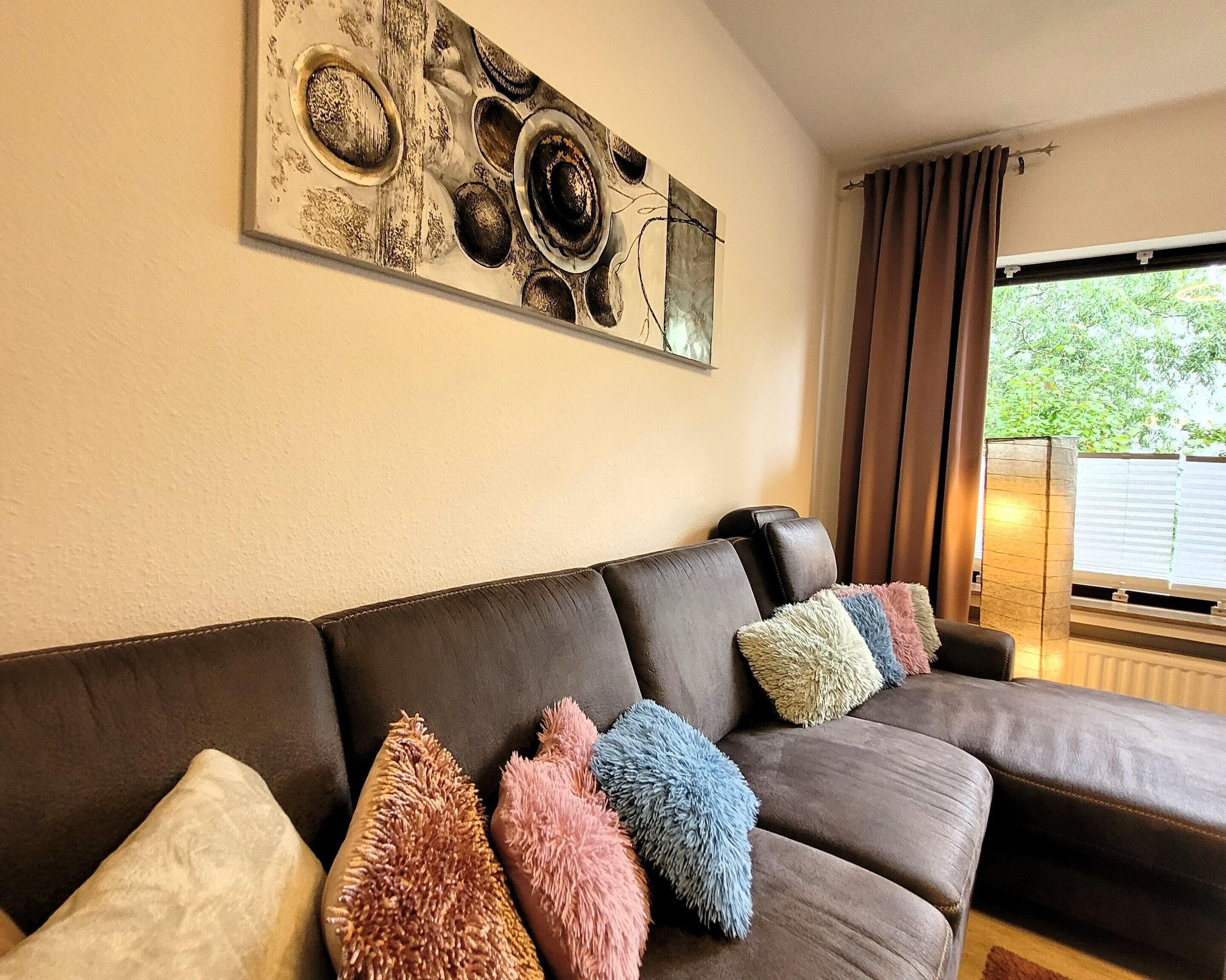 A living room with a brown leather sofa, colorful fluffy pillows, and a wall art piece.