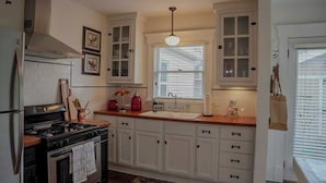 A kitchen with white cabinets, a black stove, and a window with blinds.