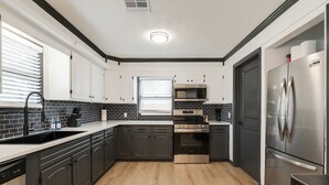 A modern kitchen with dark cabinets, a stainless steel refrigerator, a built-in oven, and a microwave.