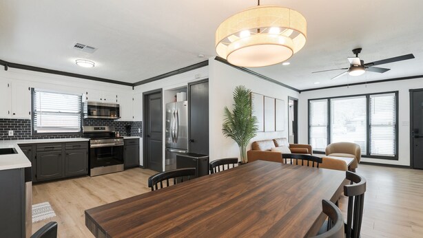 A modern kitchen with dark cabinetry, a wooden dining table, and a ceiling fan.