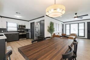 A modern kitchen with dark cabinetry, a wooden dining table, and a ceiling fan.