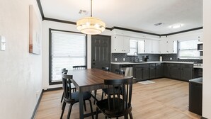 A modern kitchen with dark cabinetry, a wooden dining table, and a pendant light.