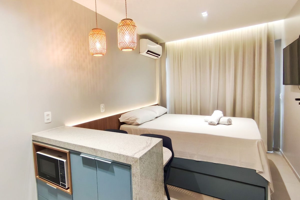 A compact hotel room with a kitchenette, a bed, a TV, and a curtain.
