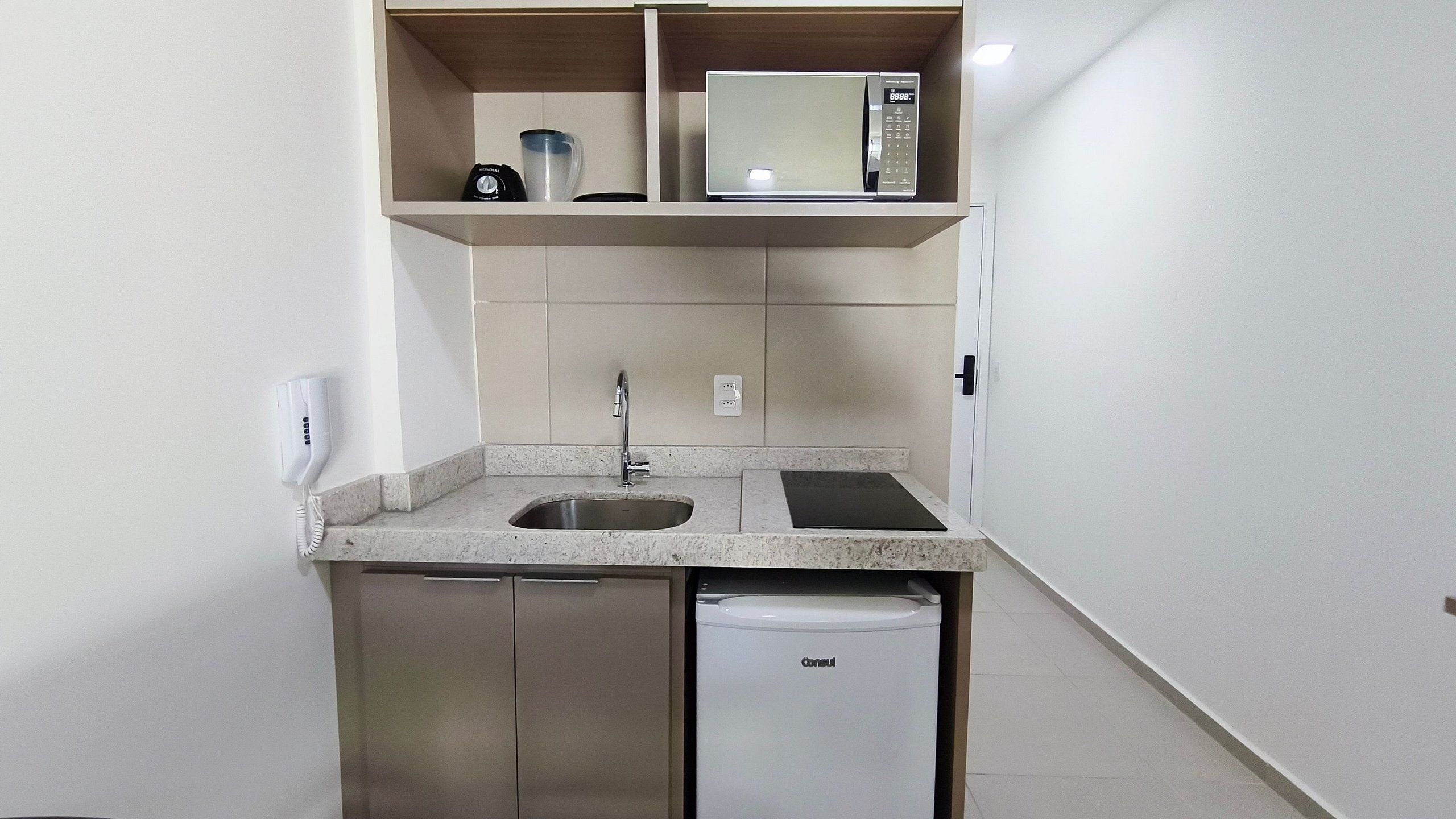 Una kitchenette compacta con microondas, lavaplatos y lavamanos.