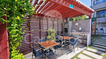 Un patio al aire libre con una parrilla, asientos y una pérgola.
