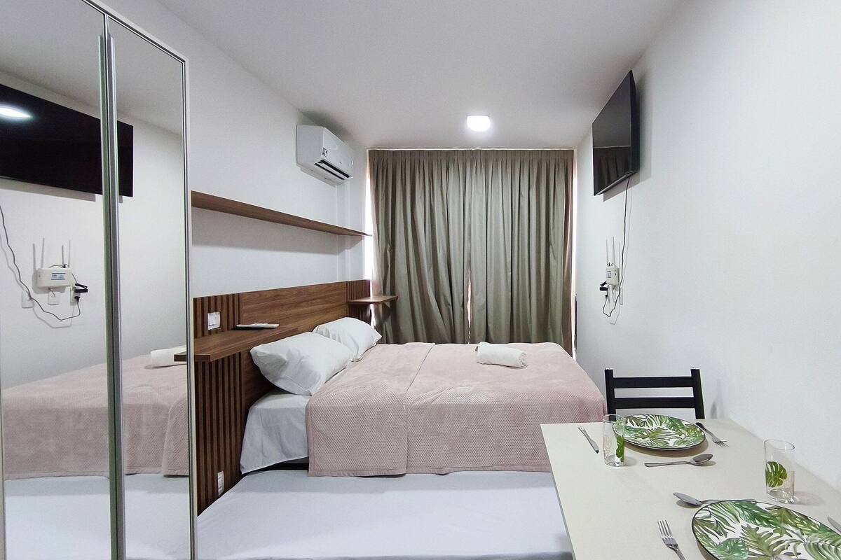 A hotel room with a bed, a bedside table with a glass of water, a chair, and a television mounted on the wall.