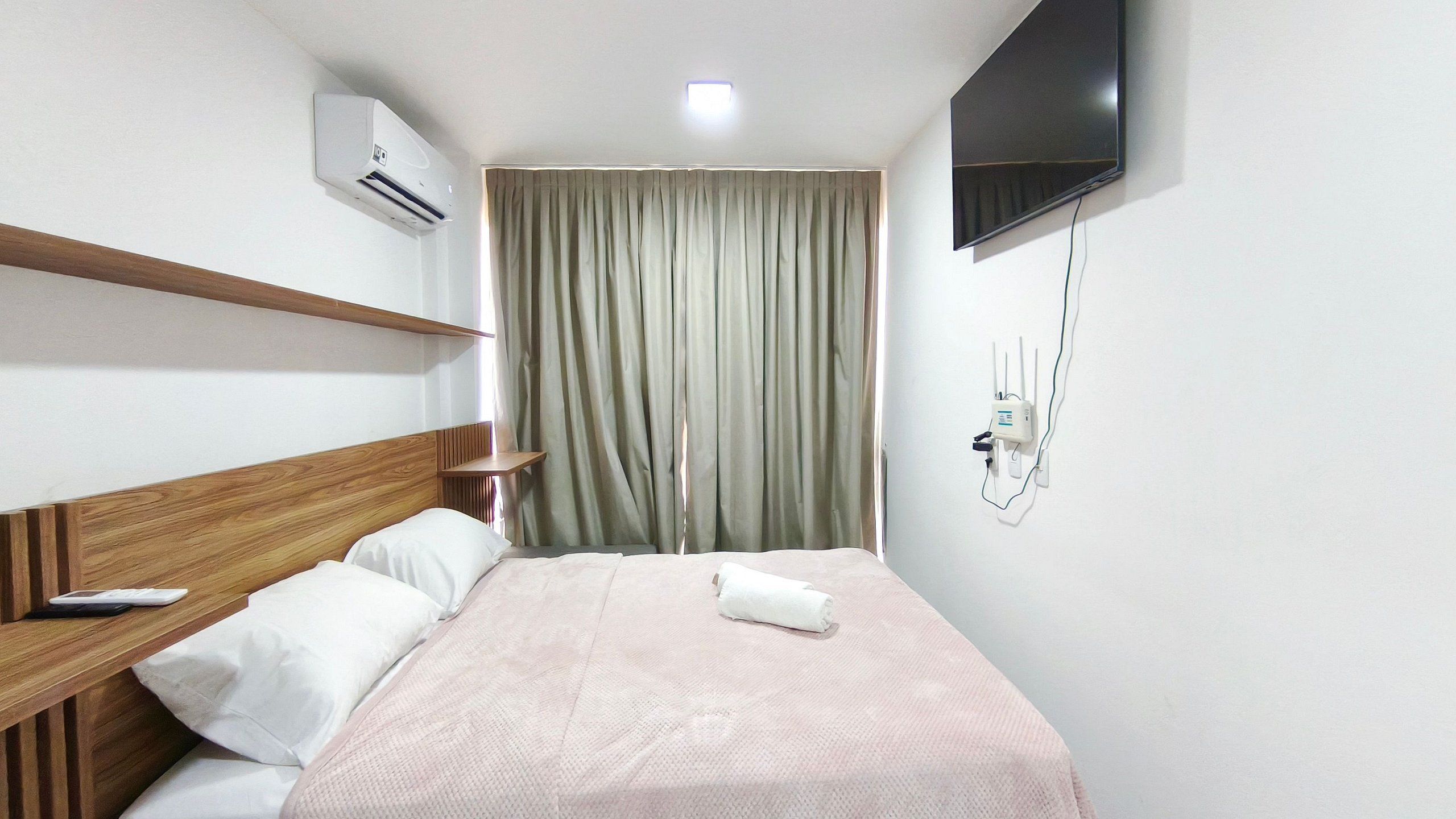 Une chambre d’hôtel équipée d’un lit, d’une télévision, d’un climatiseur et d’une prise électrique au mur.